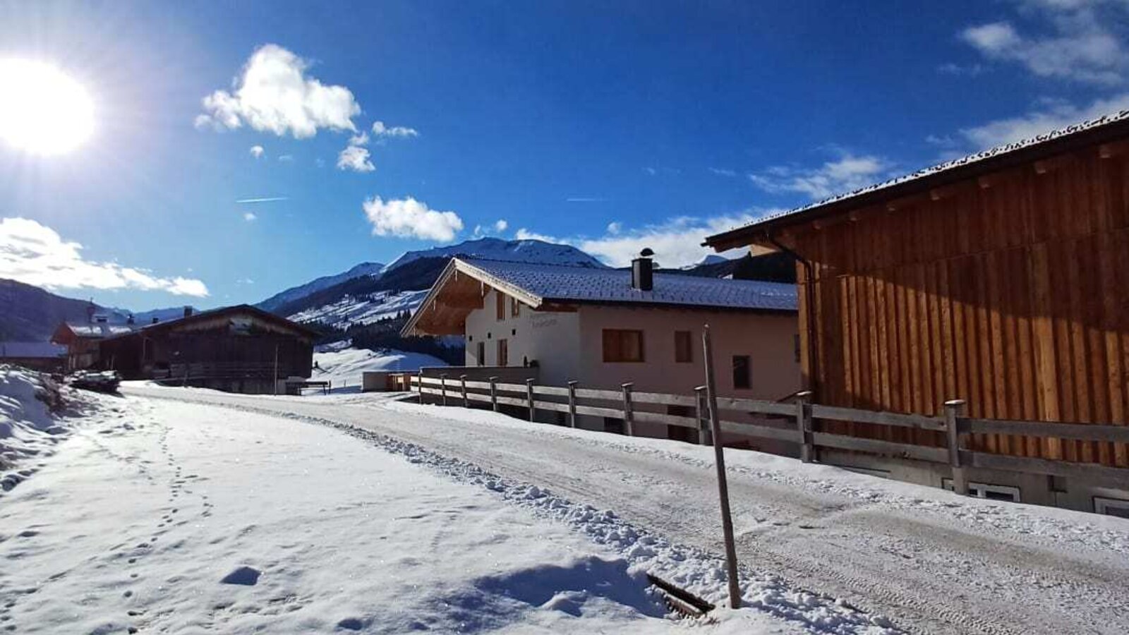 The idyllic farmhouse surrounded by a snowy winter landscape under a bright, sunny sky.