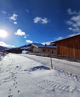 The idyllic farmhouse surrounded by a snowy winter landscape under a bright, sunny sky.