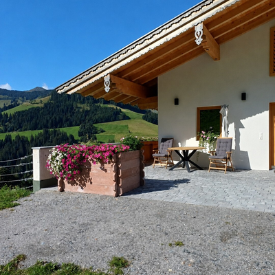The farmhouse's sunny terrace with comfortable seating, colorful flower boxes, and scenic mountain views.
