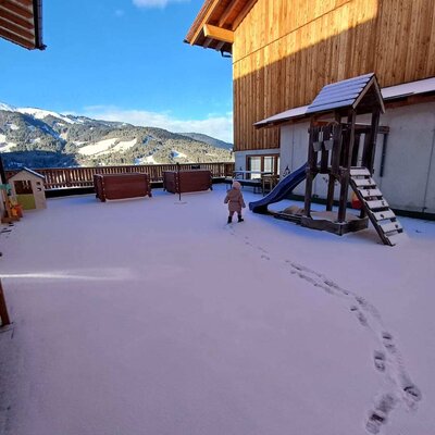 The snowy outdoor area of the Bauernhof, featuring a children's playground and mountain views.