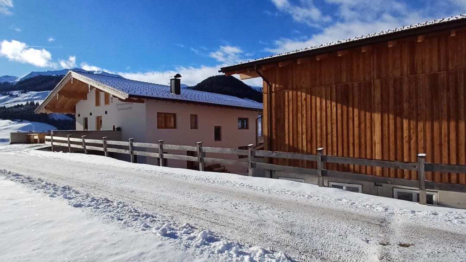 The farmhouse in winter, with a snow-covered access road and a wooden outbuilding.