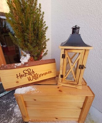 An inviting welcome at the farmhouse entrance with a rustic wooden sign, a lantern, and winter decoration.