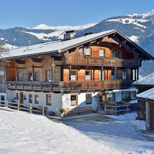 The Farm House, featuring traditional wooden architecture and multiple balconies, set amidst a snowy landscape with mountain views.