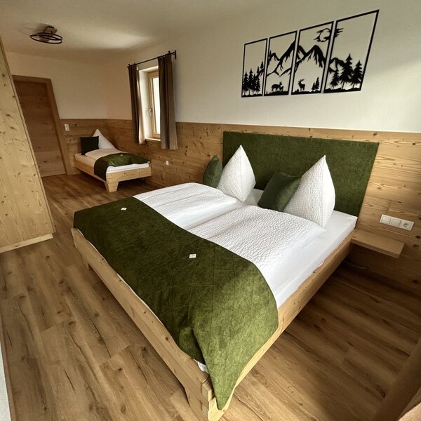Bedroom in the farm house with a double bed, a single bed, a wooden wardrobe, and wooden wall paneling.