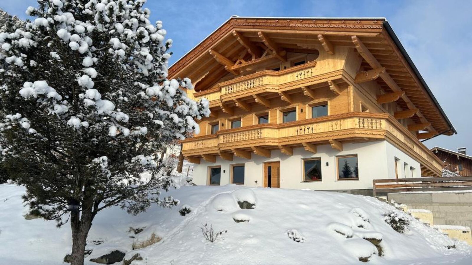 Exterior view of the farmhouse in winter, featuring a wooden facade, balconies, and snow-covered surroundings.