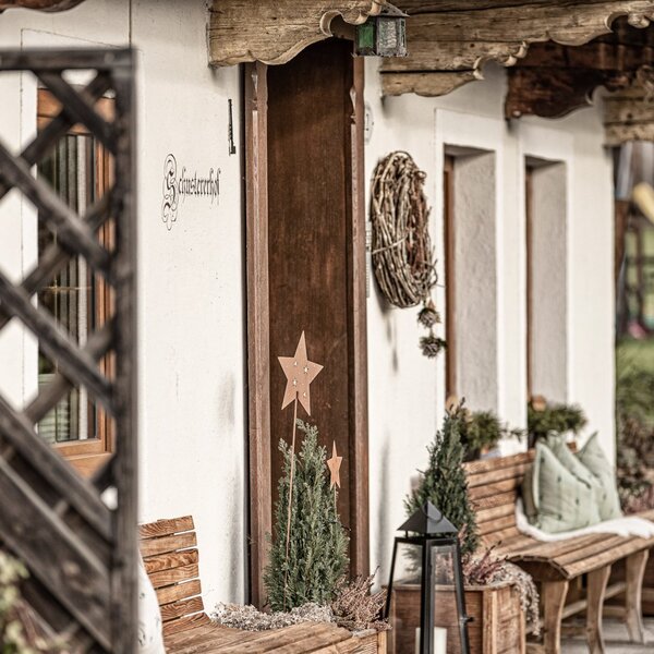 The entrance to the Farm House, identified as "Schusterhöfl," features wooden benches providing outdoor seating.