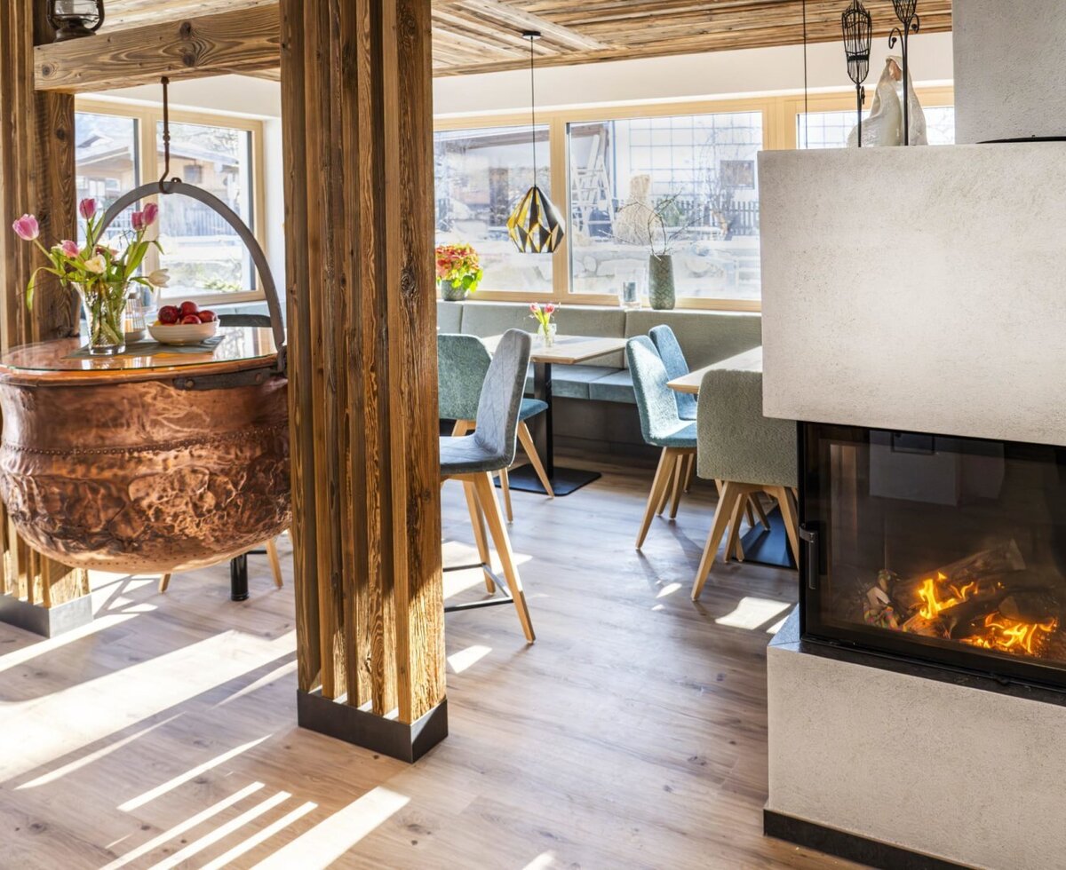 The dining area in the farmhouse, featuring a modern fireplace, a bench, chairs, and a decorative copper pot serving as a table.