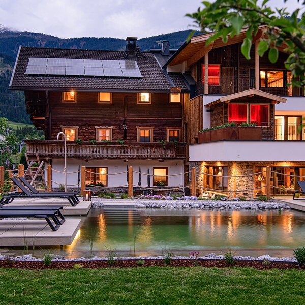 The farmhouse with a natural swimming pond and sun loungers in the garden, surrounded by the mountain landscape.