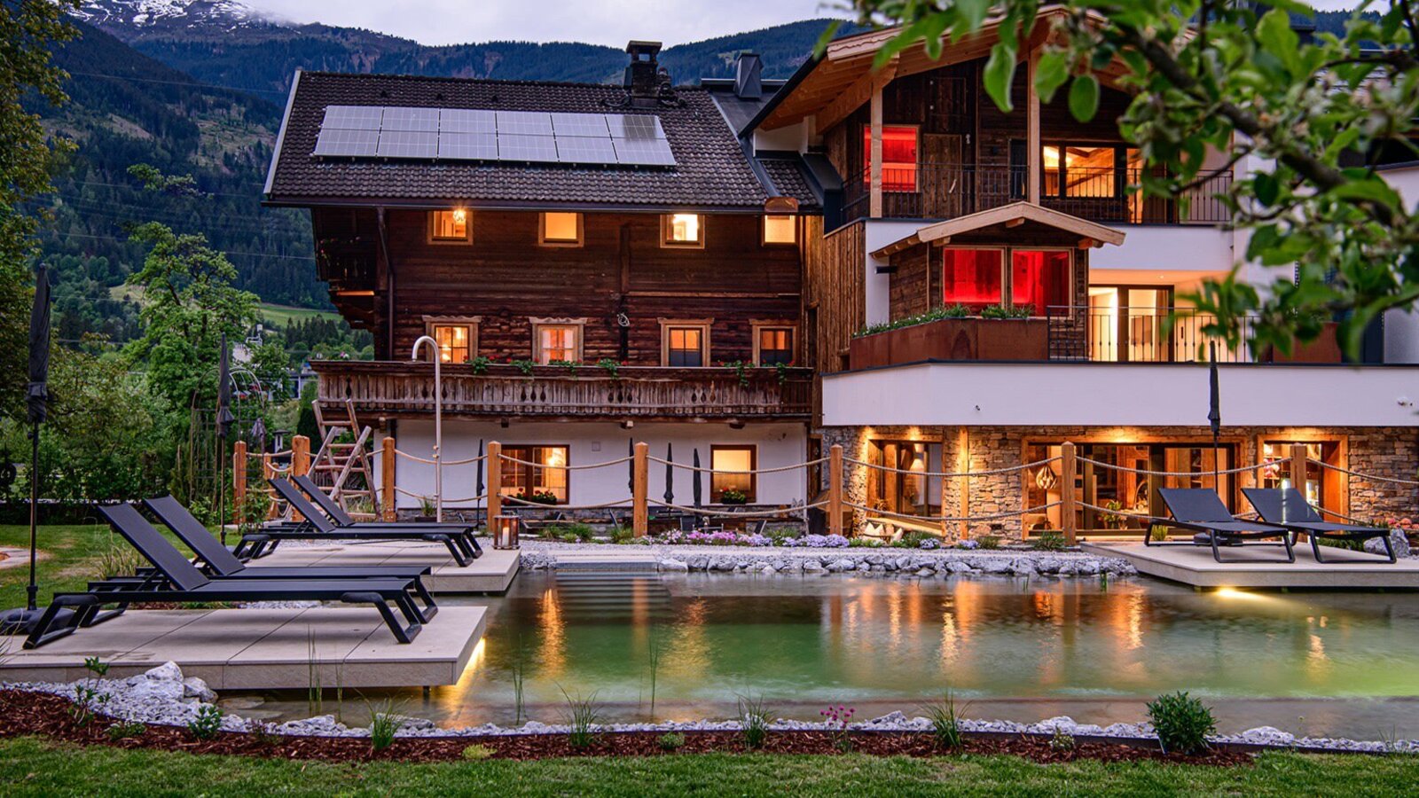 The farmhouse with a natural swimming pond and sun loungers in the garden, surrounded by the mountain landscape.