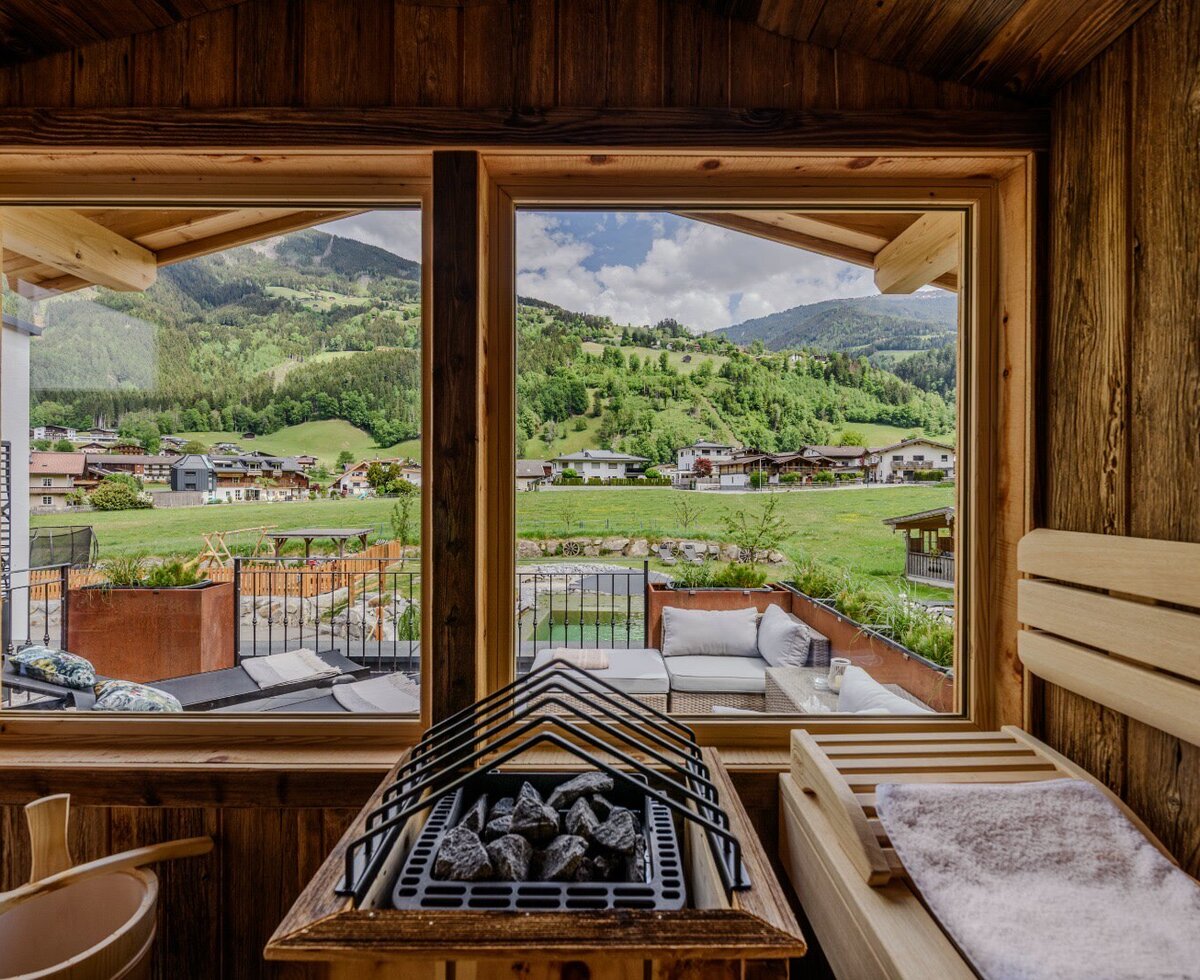 Sauna in the farmhouse with wooden interior, sauna heater, and a view of the mountains and village.