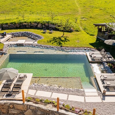 The natural swimming pond at the farmhouse, featuring sun loungers, umbrellas, and an outdoor seating area in the garden.