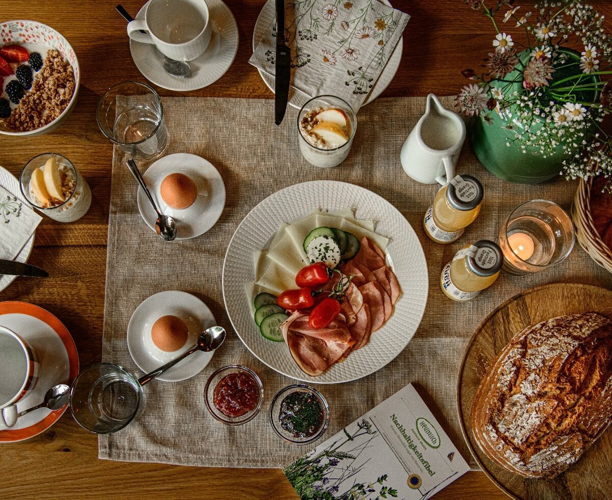 Breakfast table at the farmhouse with eggs, cold cuts, cheese, muesli, bread, and drinks.