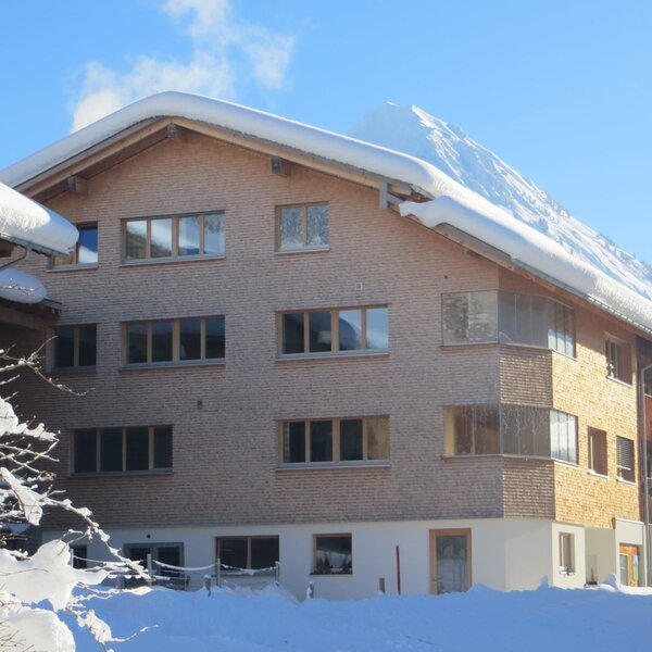 The snow-covered exterior of the Farm House, featuring a wooden facade, multiple windows, and balconies, with mountains in the background. The snow-covered exterior of the Farm House, featuring a wooden facade, multiple windows, and balconies, with mountains in the background.