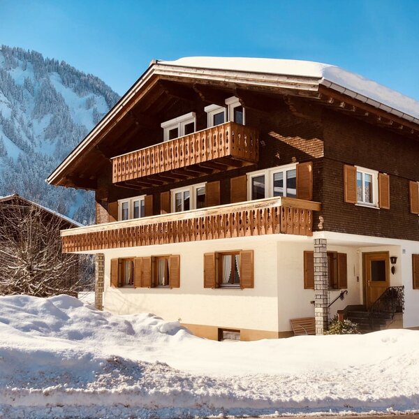The exterior of the farm house, featuring balconies and a snow-covered mountain backdrop.