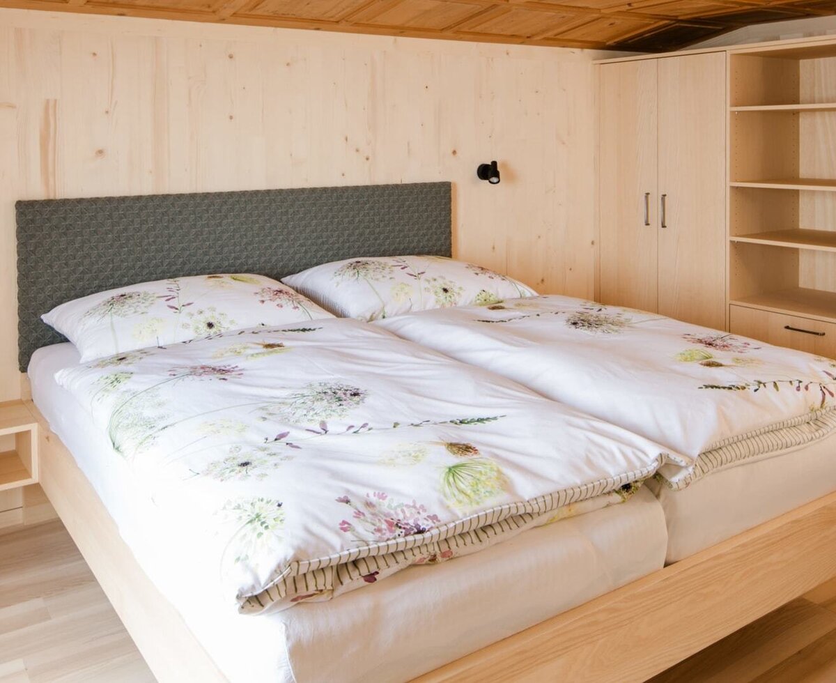Double bedroom in the Farm House, furnished with a wooden bed frame, two separate duvets, integrated bedside tables, and a built-in wooden wardrobe with shelving.