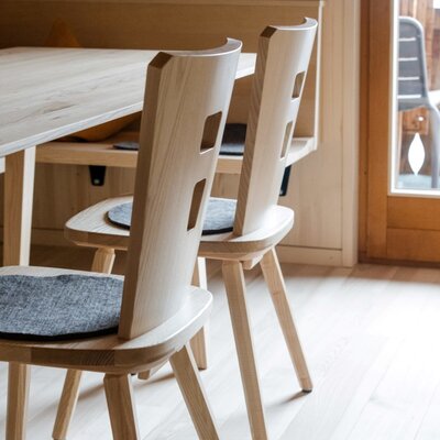 The farmhouse's dining area features a wooden table, chairs with grey felt cushions, and a built-in wooden bench.