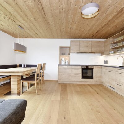 The large kitchen/living room in the Farm House features a well-equipped kitchen with an oven and coffee machine, alongside a dining area with a wooden table and corner bench.