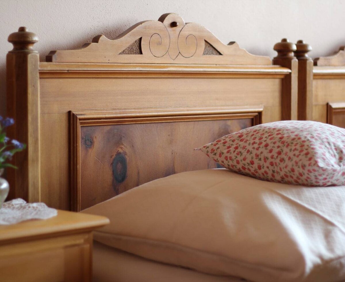 Bedroom in an apartment at the Farm House, featuring a carved wooden bed frame, pillows, and a nightstand with a vase of flowers.