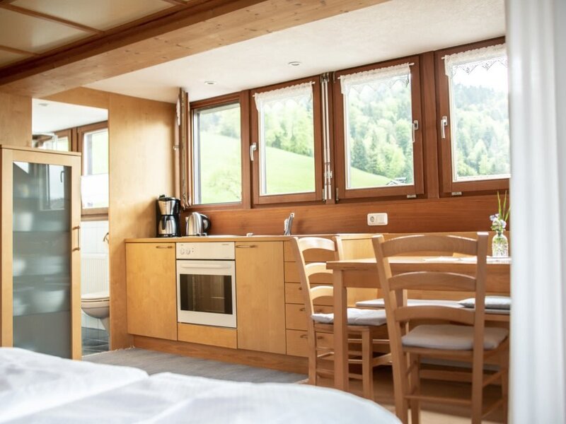 The apartment's kitchen and dining area in the Farm House features an oven, coffee maker, wooden dining table, and windows with mountain views.