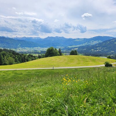 Panoramic view from the farmhouse over green hills, a road, and a valley with mountains in the background.