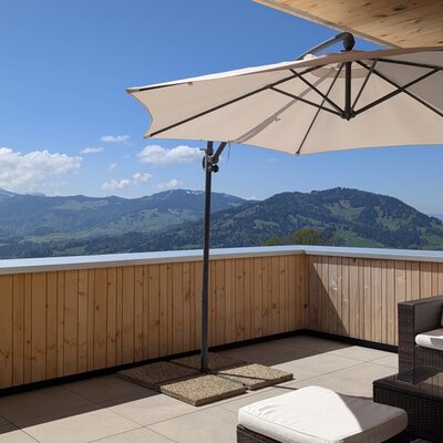 The farmhouse's sunny terrace with comfortable lounge furniture, a large parasol, and wide views of the surrounding mountains.