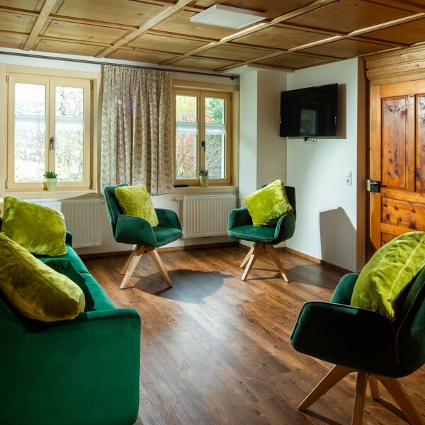 The reading room in the farm house, featuring a television, a green sofa, and armchairs. The reading room in the farm house, featuring a television, a green sofa, and armchairs.