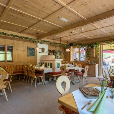 The farmhouse's rustic dining area featuring traditional wood paneling, a classic tiled stove, and inviting, set tables.