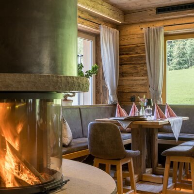 A cozy dining area at the farmhouse featuring an inviting fireplace, rustic wooden walls, and views of the green surroundings.
