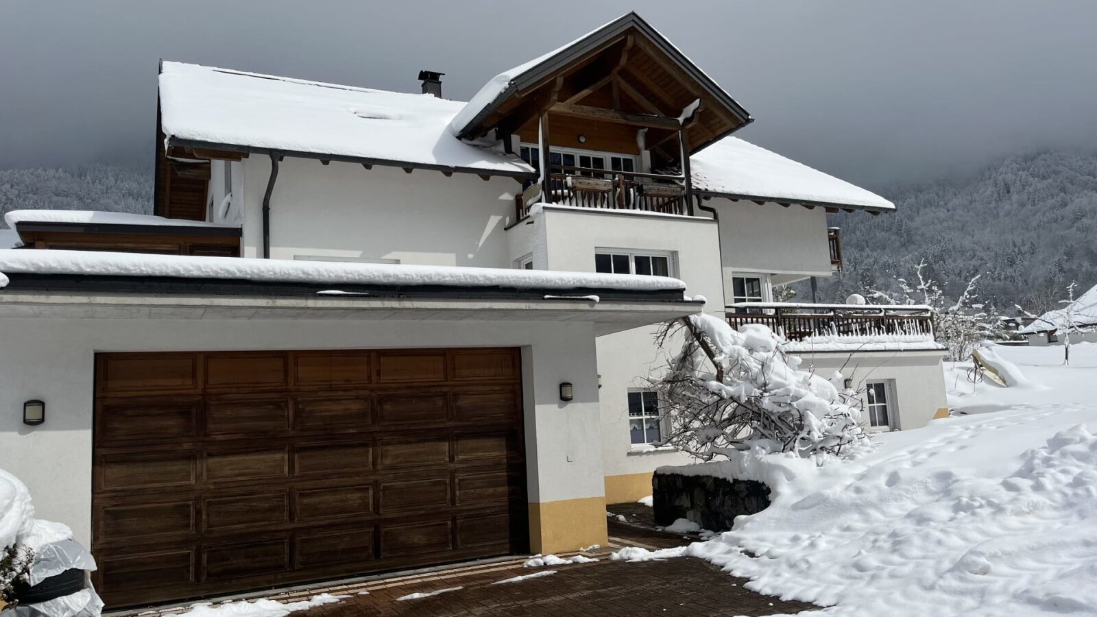 Exterior view of the farmhouse in winter with a snow-covered roof, balconies, and a wooden garage door.
