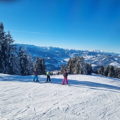 Ski slope with skiers and a snow-covered mountain landscape near the farmhouse.