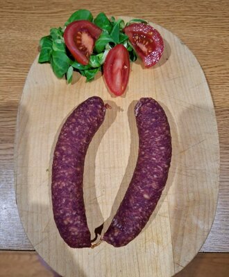 Two sausages on a wooden board, served with lamb's lettuce and tomato slices, as a culinary offering of the farmhouse.