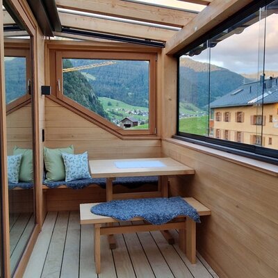 The farmhouse's glazed balcony with wooden furnishings, dining table and mountain views of the surrounding countryside.