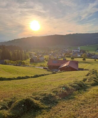 The surrounding landscape of the Farm House, featuring green hills, a distant village with a church, and the sun setting over the horizon.
