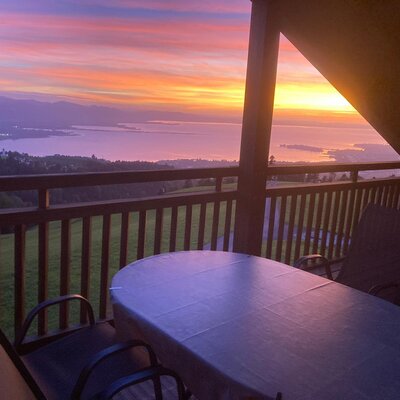 The farmhouse apartment's inviting balcony with a table, chairs, and scenic views of the lake at sunset.