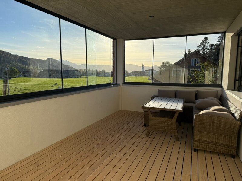 An inviting, glass-enclosed balcony featuring a comfortable seating area