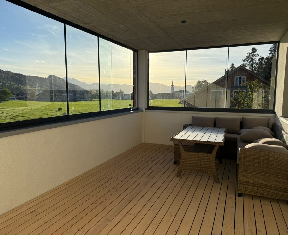 An inviting, glass-enclosed balcony featuring a comfortable seating area