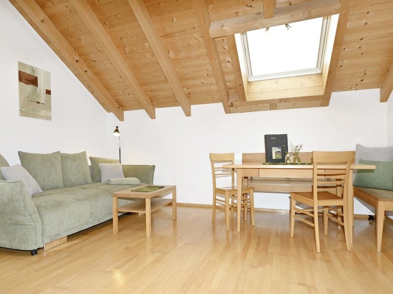 Living area of the apartment featuring a sofa, dining table with chairs and a bench, wooden beamed ceiling, and a skylight.