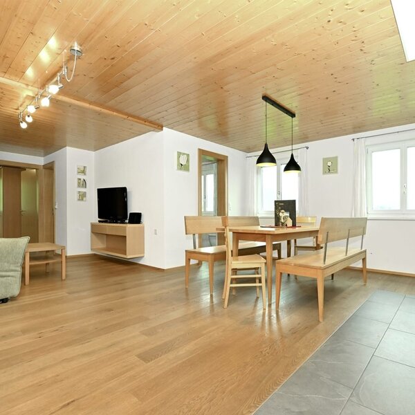 The open-plan living area of the apartment, featuring a sofa, TV, dining table, and the fully equipped living kitchen.