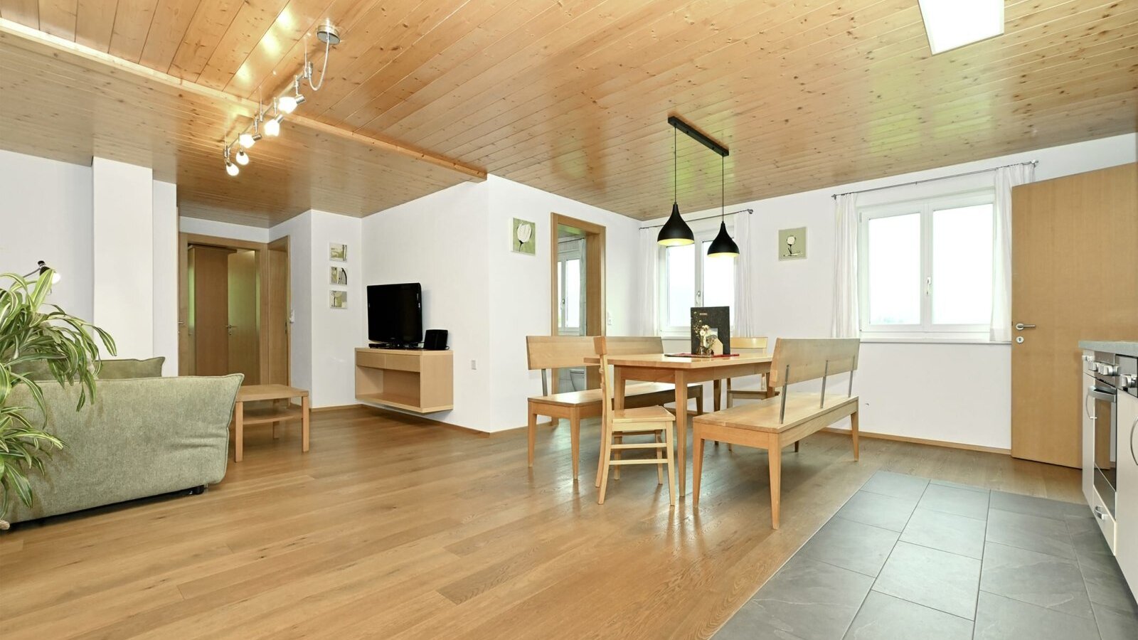 The open-plan living area of the apartment, featuring a sofa, TV, dining table, and the fully equipped living kitchen.
