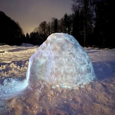 A beautifully illuminated igloo in the snowy outdoor area of the apartment at night.