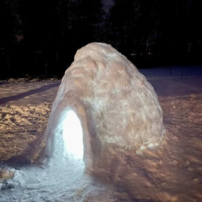 An atmospherically illuminated igloo in the snowy outdoor area of the apartment at night.