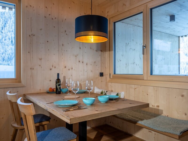 The bed and breakfast's cozy dining area featuring a modern wooden table, comfortable bench seating, and a warm pendant light with snowy views.