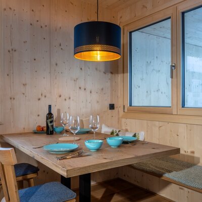 The bed and breakfast's cozy dining area featuring a modern wooden table, comfortable bench seating, and a warm pendant light with snowy views.