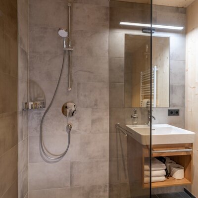 A modern bathroom featuring a walk-in shower, a light wood vanity, and stylish grey tiling.