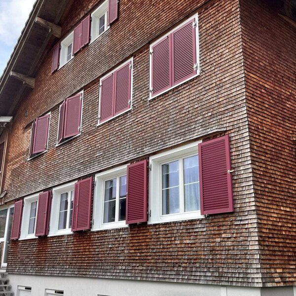 Exterior view of the farmhouse with a wooden shingle facade, white windows, and red shutters.