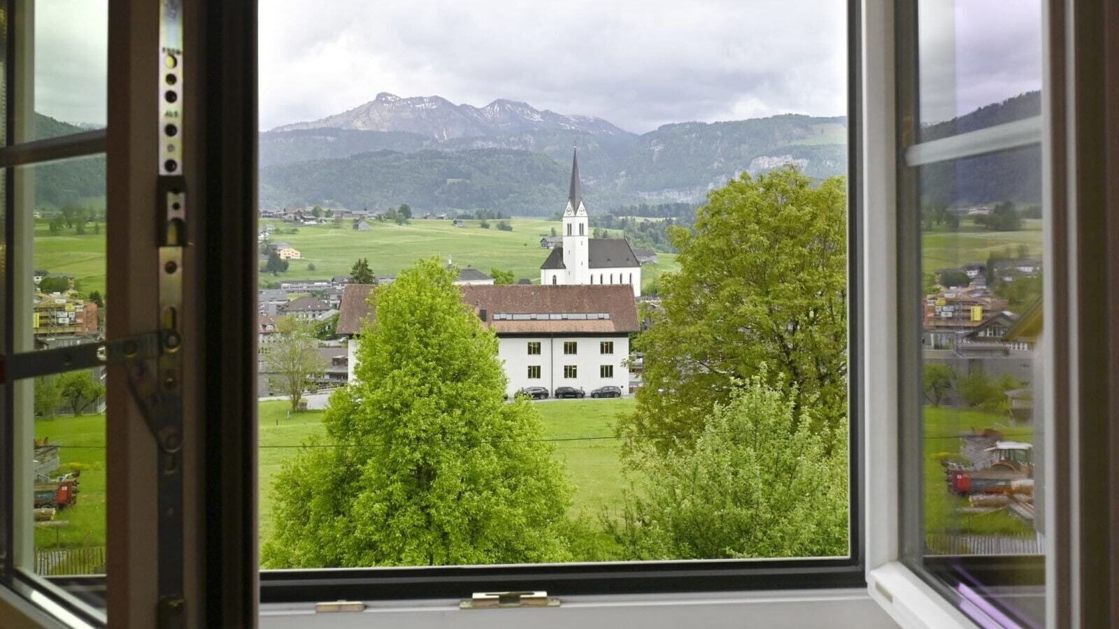 View from the farmhouse window of the village with a church and the surrounding mountain landscape.