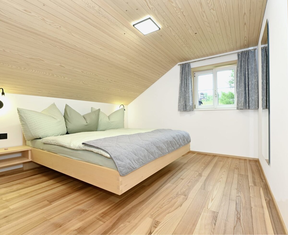 Bedroom in the farmhouse featuring a double bed, wood-paneled sloped ceiling, and wooden flooring.