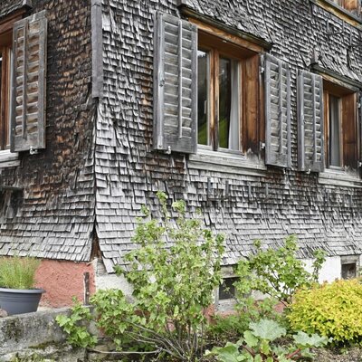 The exterior of the farmhouse, featuring traditional wooden shingle siding and multiple windows with shutters.