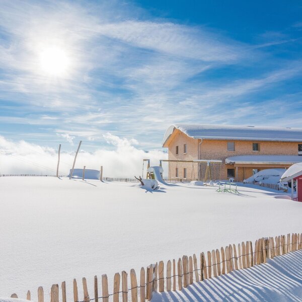 The snow-covered grounds of the Farm House feature a children's playground with swings, a slide, and a red playhouse.