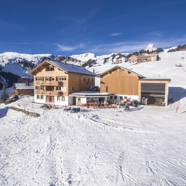 The farmhouse sits directly on a snowy ski slope, offering an outdoor terrace for guests to relax.